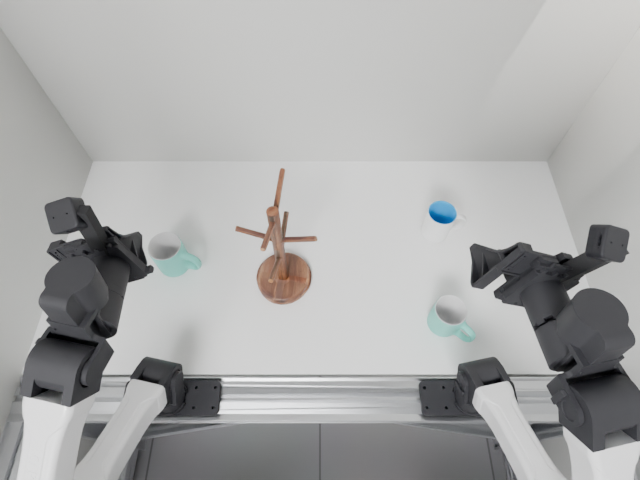 Overhead observation: three mugs, a wooden rack, and two robot arms.